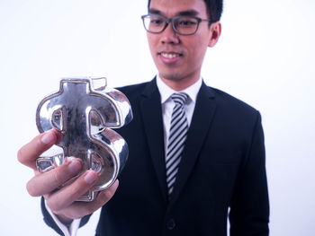 Portrait of young man holding eyeglasses against white background