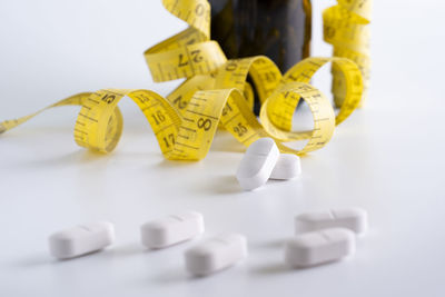 Close-up of medicines and tape measure over white background