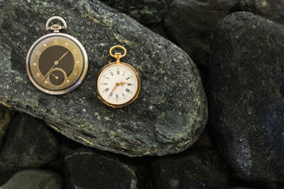 Set of watches on wet green stones with a gold pocket watch and a black and silver pocket watch