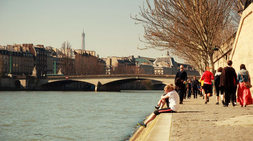 People walking by seine river in city against sky