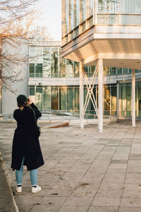 Rear view of woman walking on footpath against building