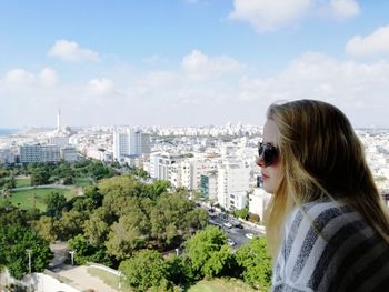 Young woman looking at cityscape against sky
