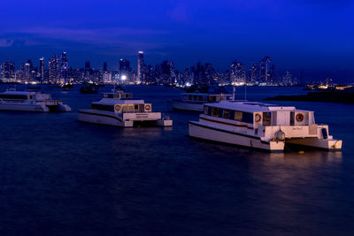 Boats moored in sea against illuminated buildings at dusk