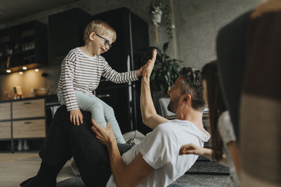 Happy son giving high-five to father while sitting on lap at home