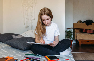 The girl after school plays at home, draws with pencils and felt-tip pens