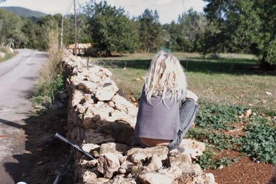 Rear view of girl sitting on stones against trees