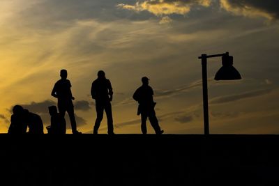 Silhouette people walking on retaining wall against sky during sunset