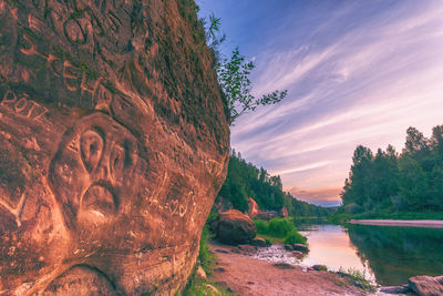Rock formation by lake against sky during sunset