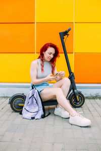 Woman uses a smartphone and an electric scooter in the summer in the city