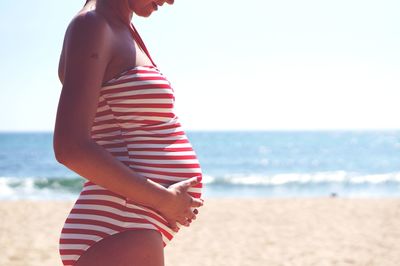 Midsection of woman standing at beach against sky