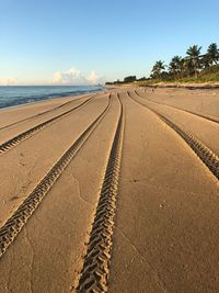 Tire tracks on road by beach against sky