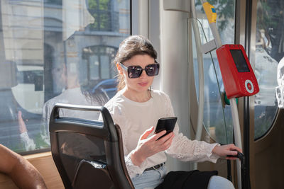 Young brunette browsing and typing messages on phone on way to work in tram
