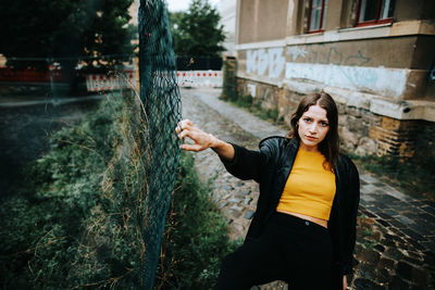 Portrait of young woman standing by fence