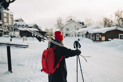 Rear view of young woman carrying skis while standing on snow during winter