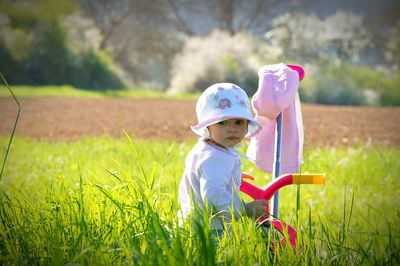 Side view of girl looking away while standing with tricycle on grassy field