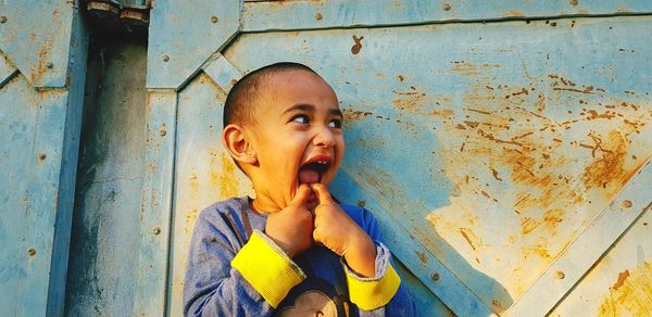 Cute boy with finger in mouth standing against metal gate