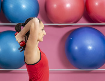 Side view of woman lifting dumbbell against fitness balls
