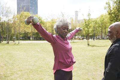 Man looking at senior woman exercising with dumbbells in park