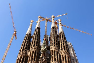 Low angle view of crane at church against clear blue sky