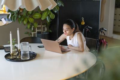 Woman with disability using laptop on dining table at home