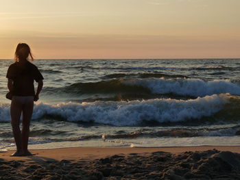 Woman standing on beach against sky during sunset