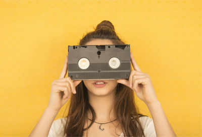 Woman holding audio cassette against yellow background