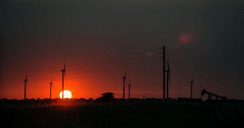 Silhouette electricity pylons on field against orange sky