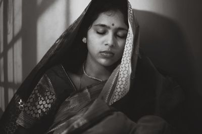 Close-up of woman with eyes closed in traditional clothing against wall