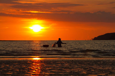 Silhouette man standing in sea against orange sky