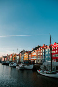 Boats moored at harbor by buildings against sky