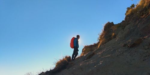 Side view of man standing on mountain against clear blue sky