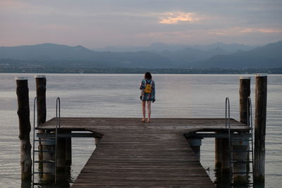 Rear view of woman standing on pier at lake