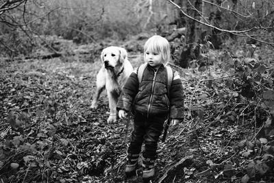 Cute boy standing with dog on field at forest