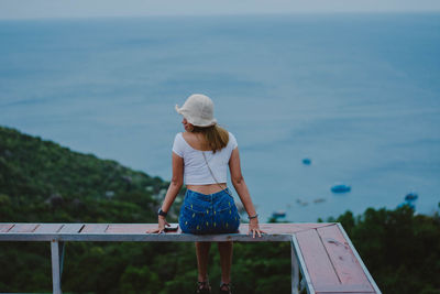 Woman sitting by sea against sky