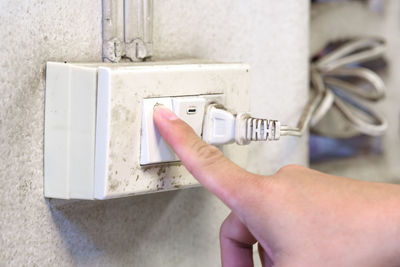 Close-up of person hand pressing push button on electrical outlet