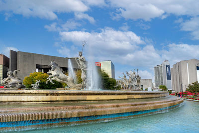 Fountain by swimming pool in city against sky