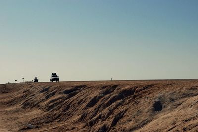 Cars moving on desert against clear sky