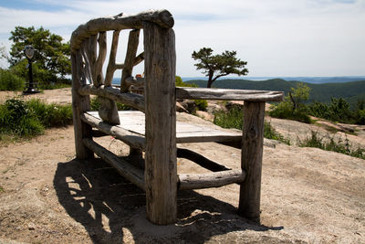 Wooden bench on field by tree against sky