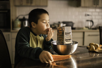 Little boy licks his fingers from carrot juice, helps mother in kitchen,  vegetables. womens day