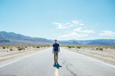 Portrait of man walking on road against sky during sunny day