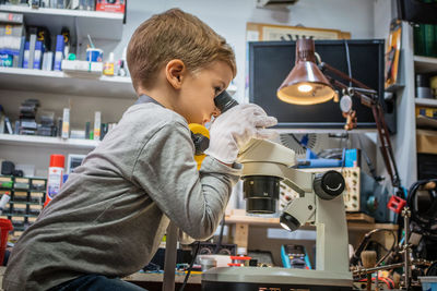 Side view of boy looking through microscope in workshop