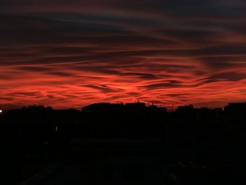 Silhouette of city against dramatic sky during sunset