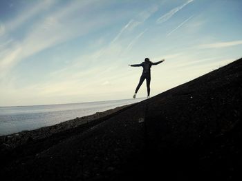 Rear view of woman with arms outstretched standing against sea at beach