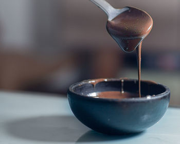 Close-up of creamy chocolate sauce dripping down from a spoon to a small ceramic bowl