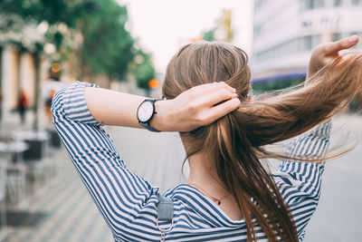 Rear view of woman tying hair while standing on road in city