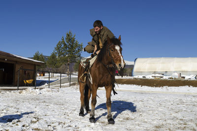 Man sitting on horse in ranch against clear sky