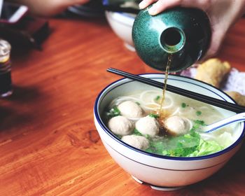 High angle view of woman pouring oil in soup bowl on table