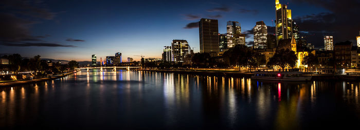 Illuminated buildings by river against sky at night