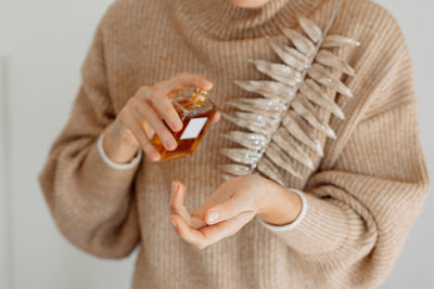 Midsection of woman spraying perfume on hand