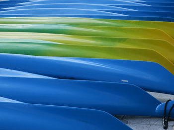 A collection of blue , yellow and green canoes laying upward down